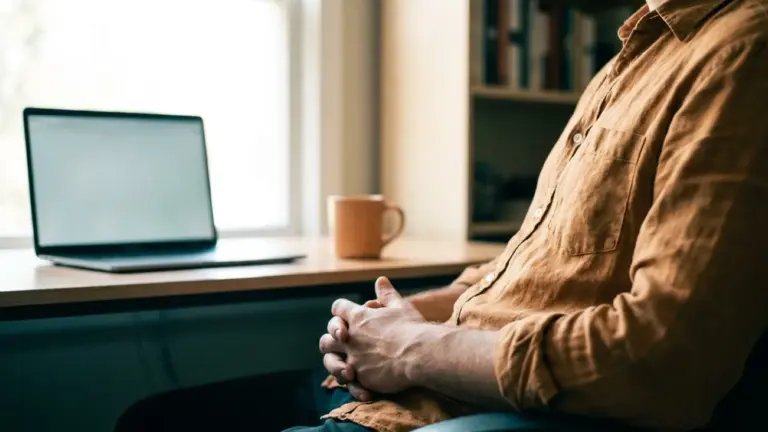 A person sitting back from an open laptop with their hands resting in their lap
