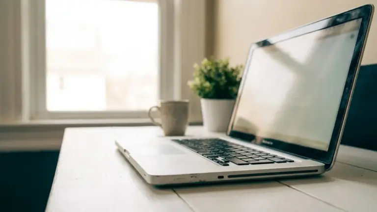 An aluminium laptop open on a desk at a low angle, catching window light