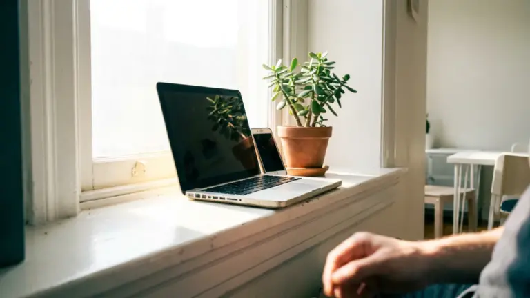 A laptop open on a broad windowsill with a phone propped against its base