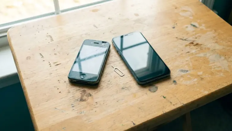 An old scuffed phone and a new one lying side by side on a pale table, a SIM tray pin between them