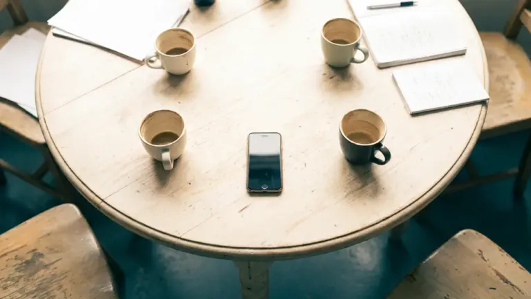 A round table seen from above with four coffee cups around it and a phone in the centre
